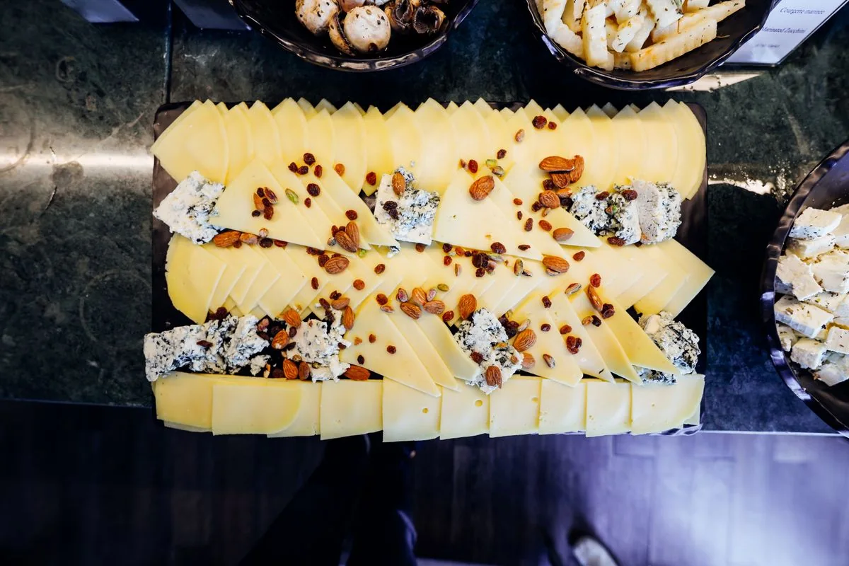 Overhead photograph of sliced cheeses arranged with nuts and dried fruit on a board