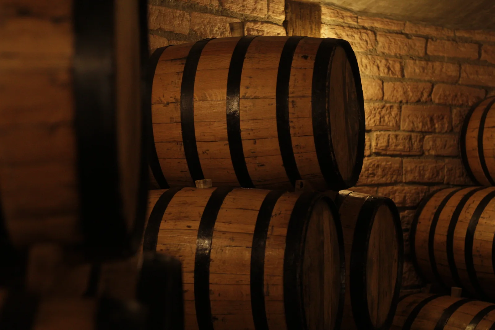 Photograph of wooden barrels stacked in a warmly lit stone cellar